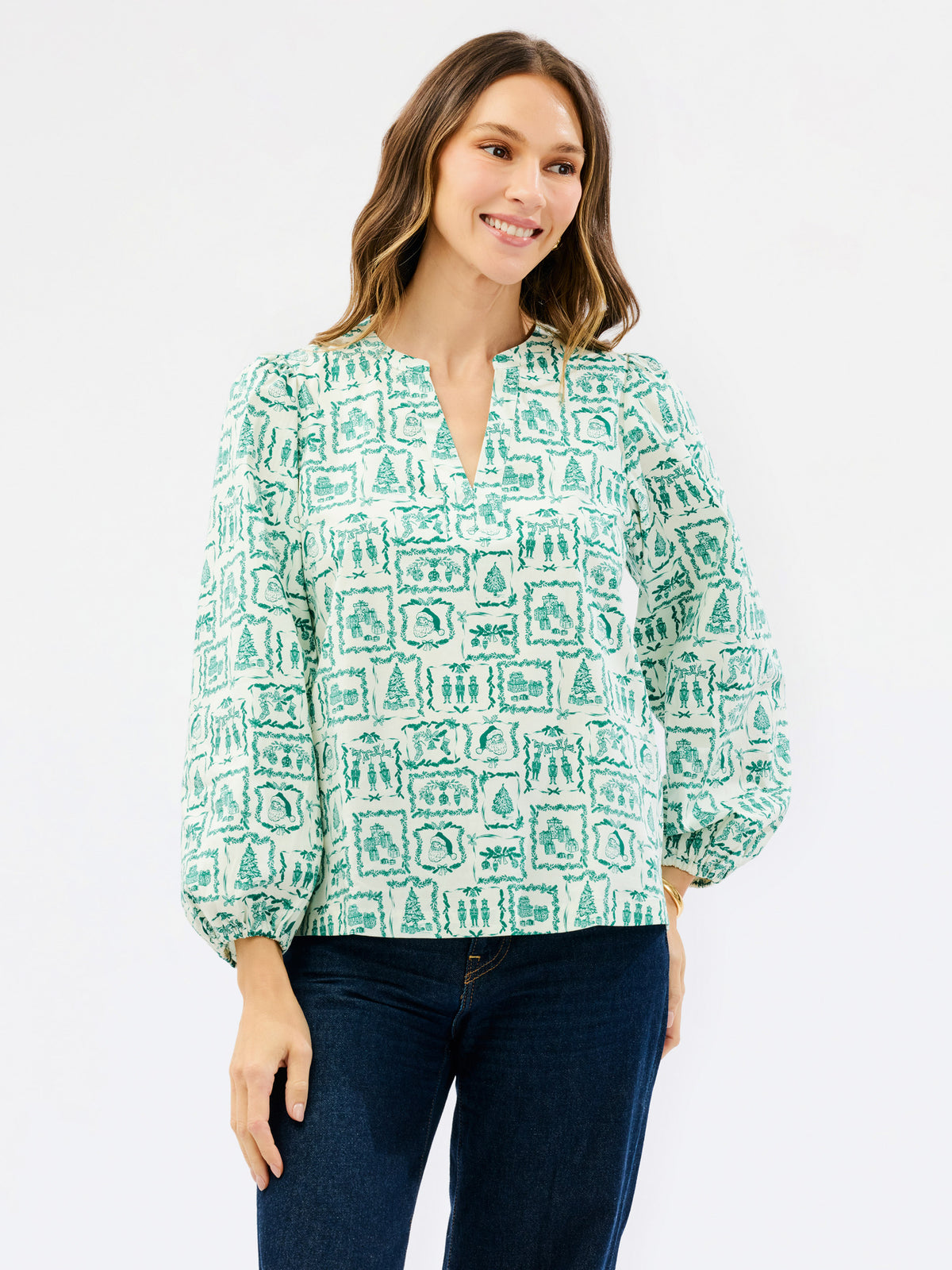 Brown haired woman wearing a white blouse with santa and other christmas icons on it 