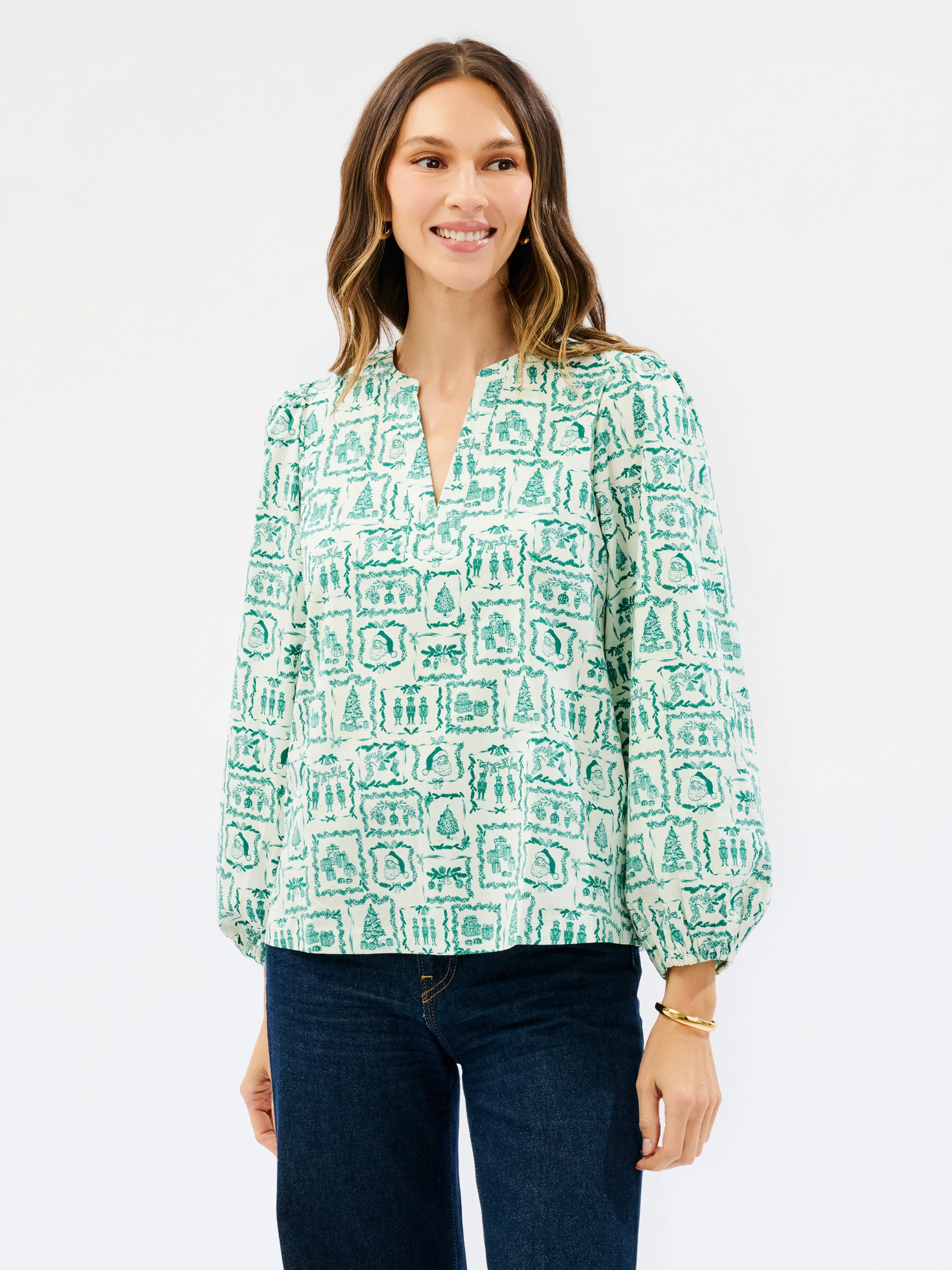 Brown haired woman wearing a white blouse with santa and other christmas icons on it 