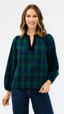 A woman wearing a long-sleeve plaid blouse in dark green and navy with a black split neckline, paired with dark blue jeans, against a plain white studio background.