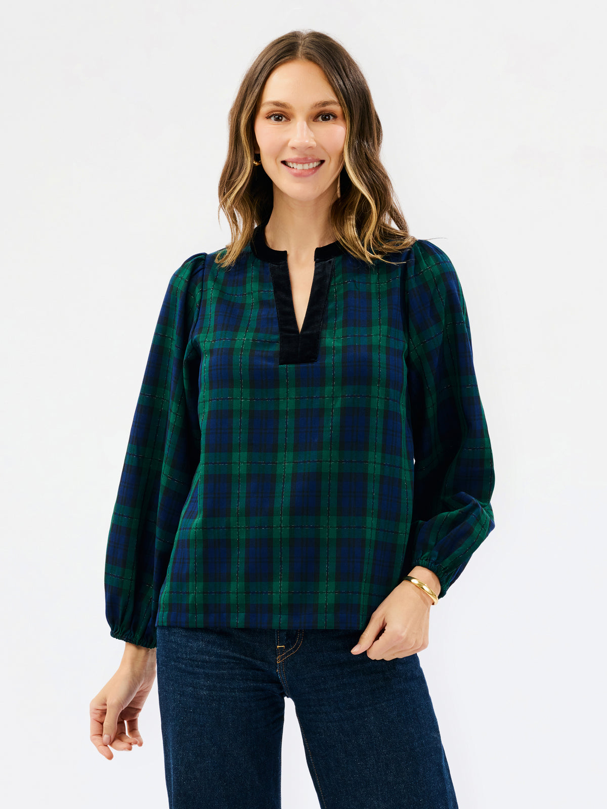 A woman wearing a long-sleeve plaid blouse in dark green and navy with a black split neckline, paired with dark blue jeans, against a plain white studio background.