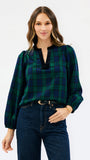 A woman modeling a long-sleeve plaid blouse in dark green and navy blue with a split neckline, paired with dark blue jeans, against a plain white studio background.