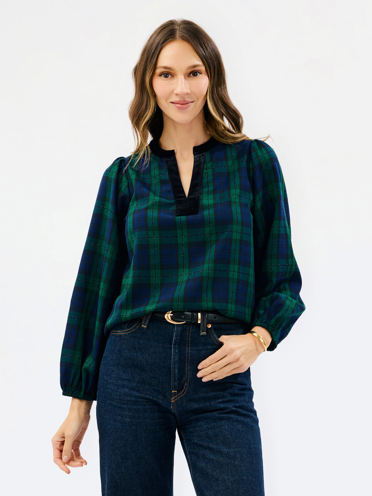 A woman modeling a long-sleeve plaid blouse in dark green and navy blue with a split neckline, paired with dark blue jeans, against a plain white studio background.