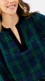 A close-up of a woman wearing a green and navy plaid long-sleeve top with a black velvet split neckline.