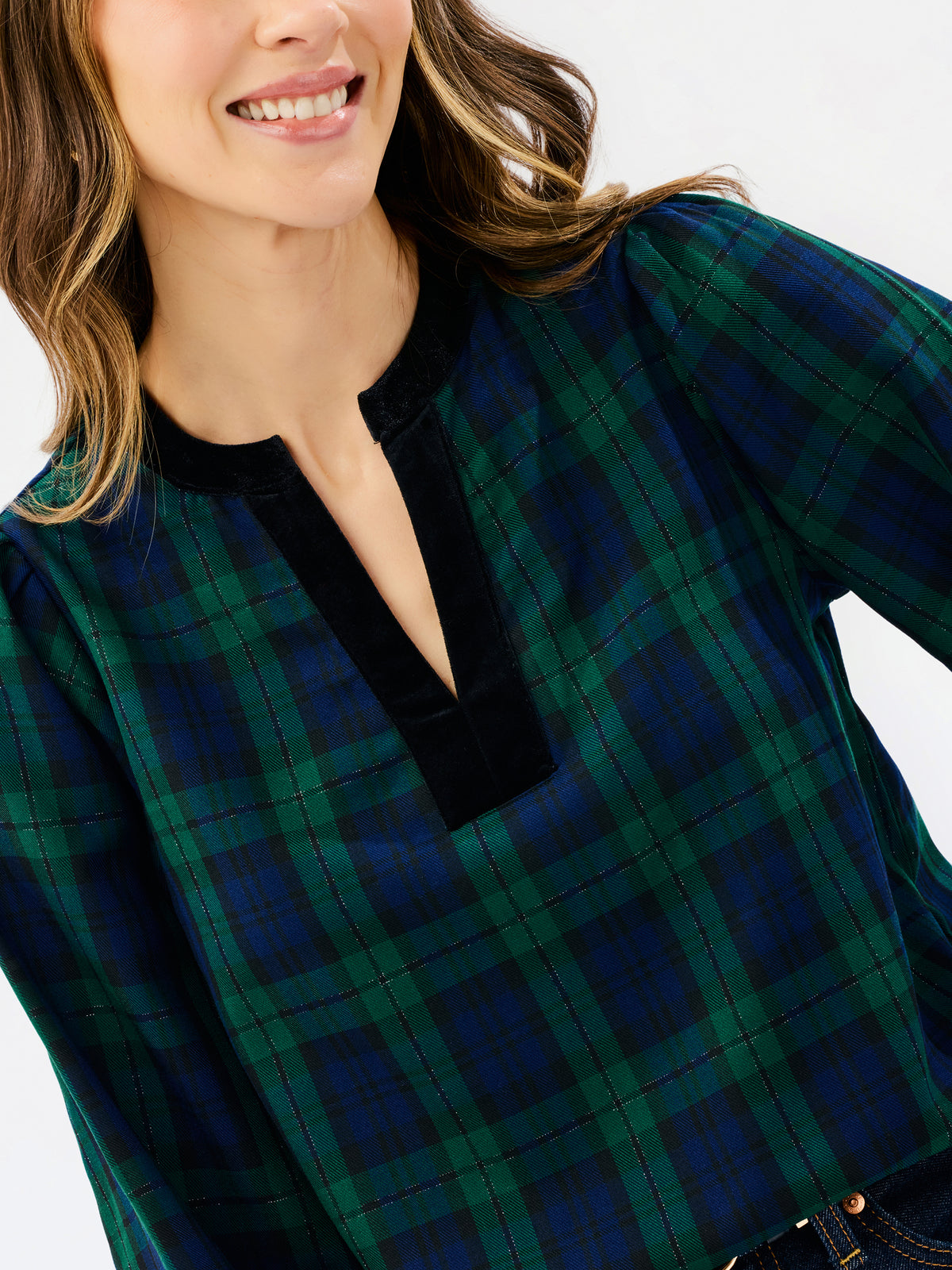 A close-up of a woman wearing a green and navy plaid long-sleeve top with a black velvet split neckline.