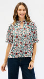 A woman modeling a short-sleeve blouse with a floral print, featuring a keyhole neckline and ruffled sleeves, paired with dark blue jeans against a plain white background.