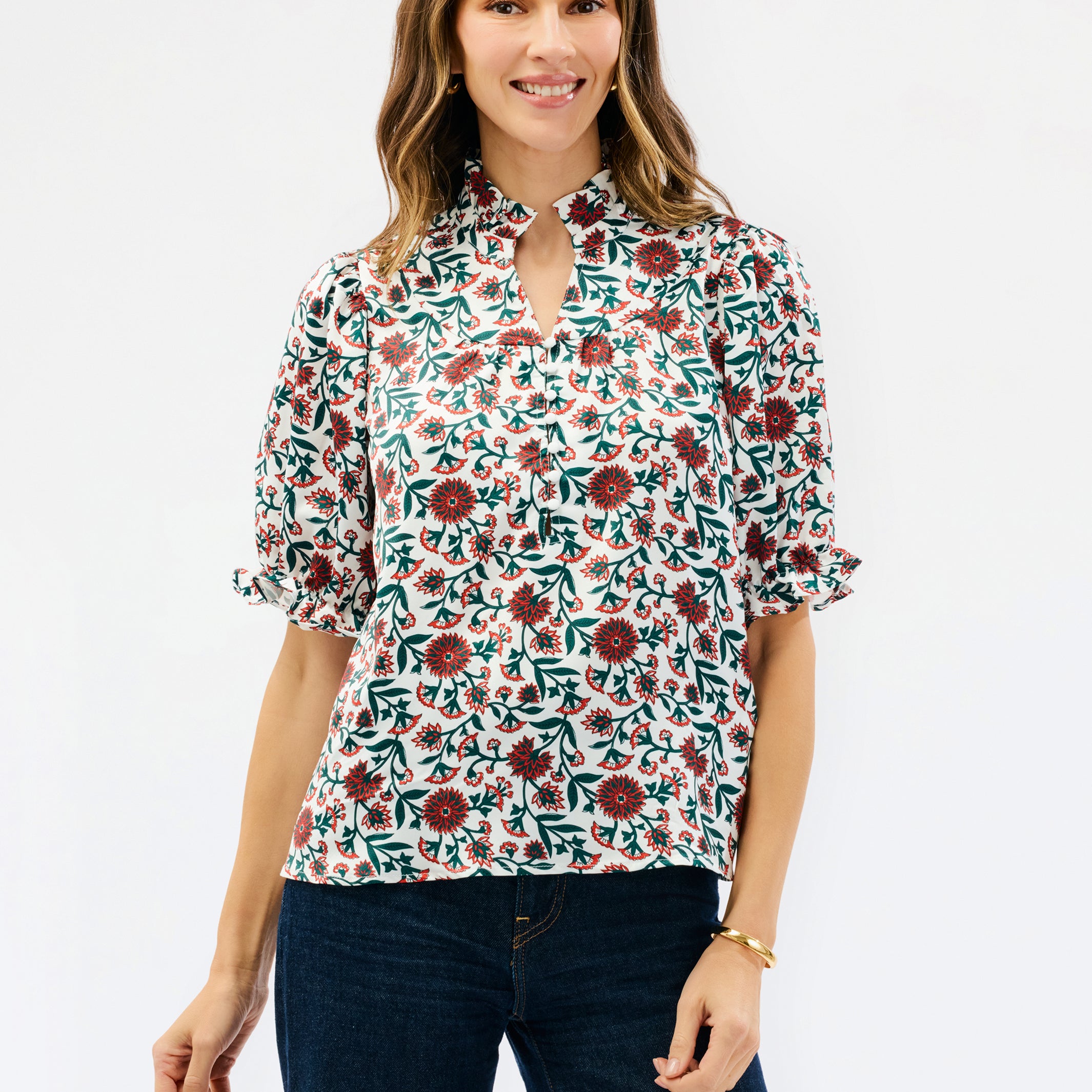 A woman modeling a short-sleeve blouse with a floral print, featuring a keyhole neckline and ruffled sleeves, paired with dark blue jeans against a plain white background.