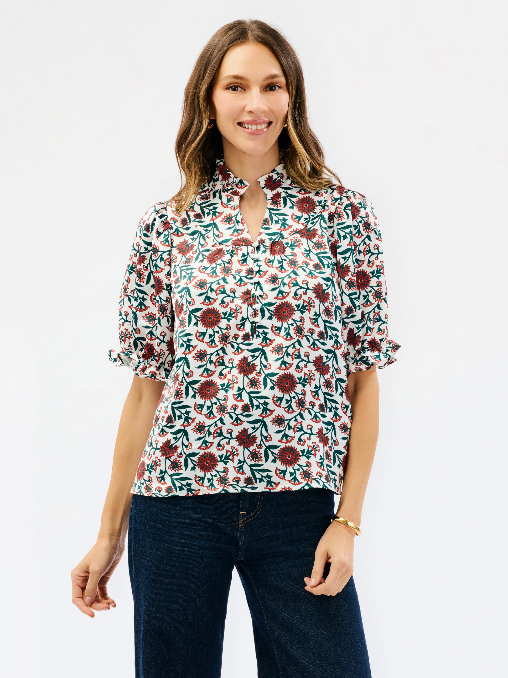 A woman modeling a short-sleeve blouse with a floral print, featuring a keyhole neckline and ruffled sleeves, paired with dark blue jeans against a plain white background.