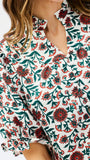 A close-up of a woman wearing a short-sleeve blouse with a white base and an allover floral print in dark green and red-orange.