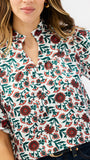 A woman wearing a white short-sleeve button-up blouse with a red and green floral print, paired with dark blue jeans.