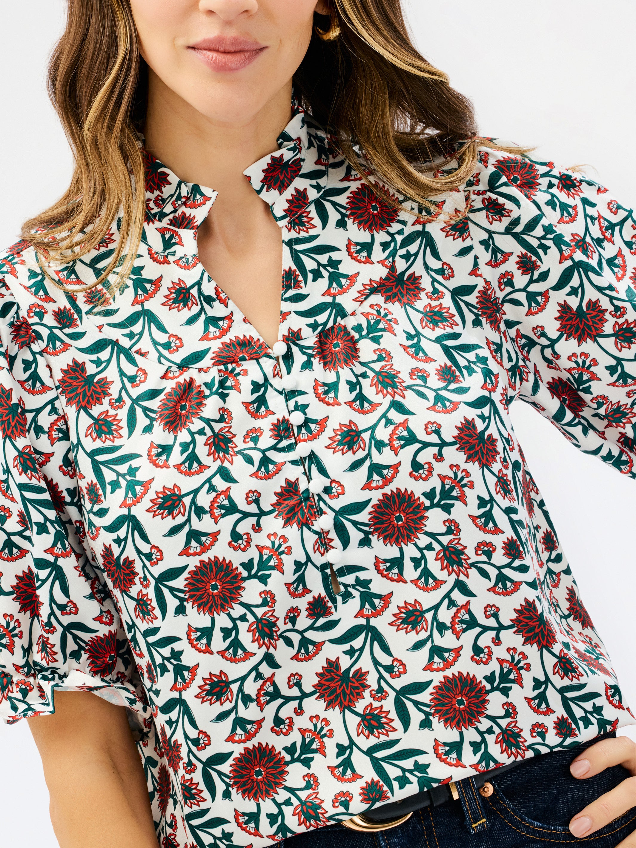 A woman wearing a white short-sleeve button-up blouse with a red and green floral print, paired with dark blue jeans.