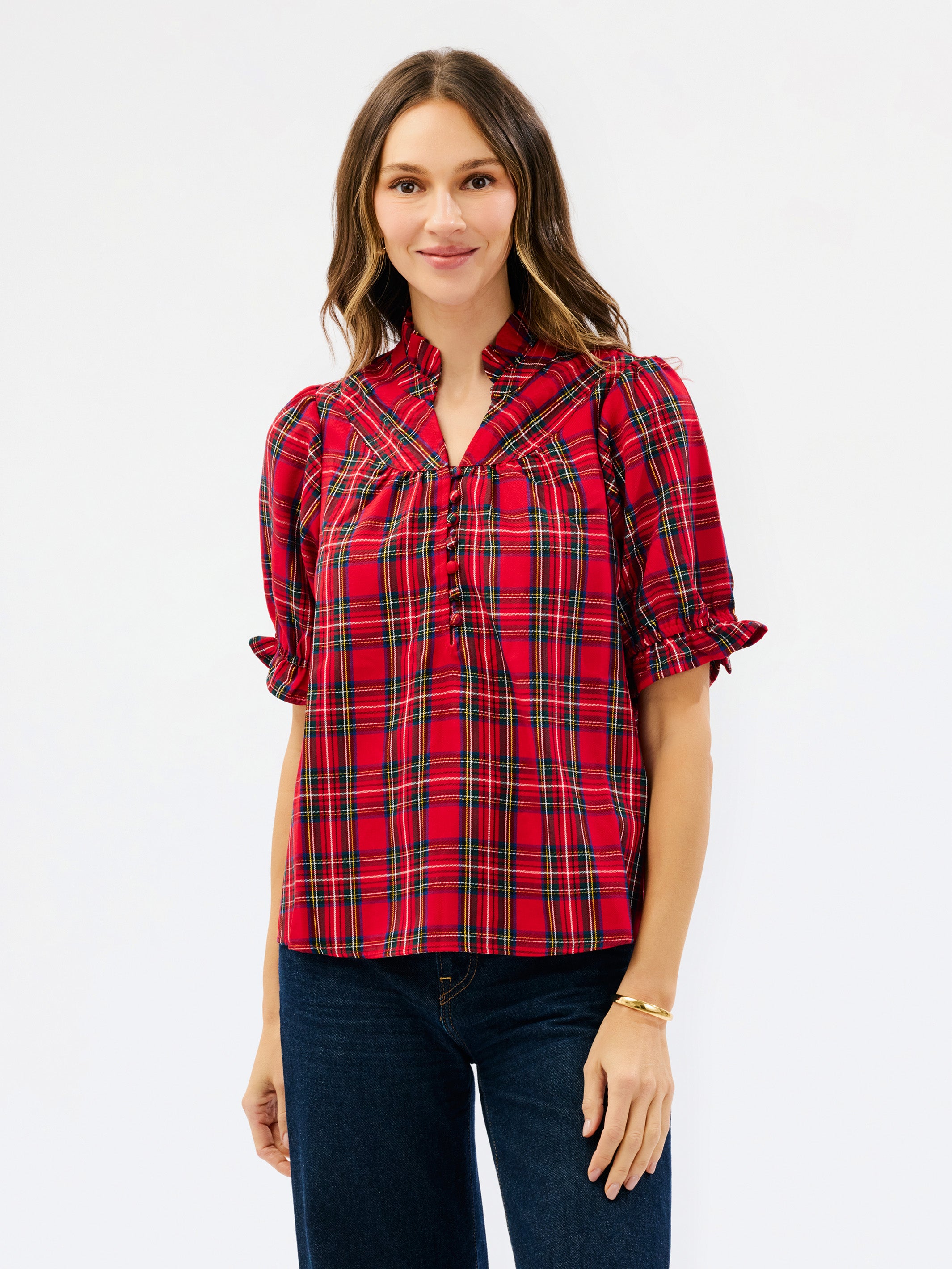 A woman modeling a red plaid short-sleeve blouse with a gathered chest detail and dark blue jeans, set against a plain white studio background.