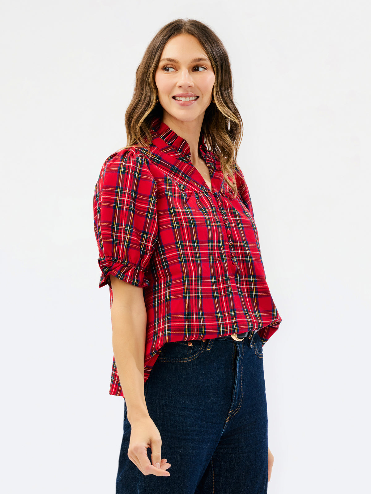 A woman modeling a red and black plaid short-sleeve button-up shirt with dark blue jeans, photographed against a plain white studio background.