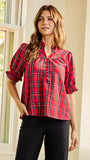 A woman modeling a red and black plaid short-sleeve blouse with a button-down front and ruffled sleeves, paired with black pants, standing in a brightly lit indoor setting.