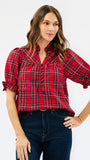A woman wearing a red and black plaid short-sleeve blouse with puff sleeves and dark blue jeans, standing against a plain white studio background.