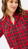 A woman wearing a red plaid button-up blouse with green and yellow intersecting lines, photographed against a plain light background.