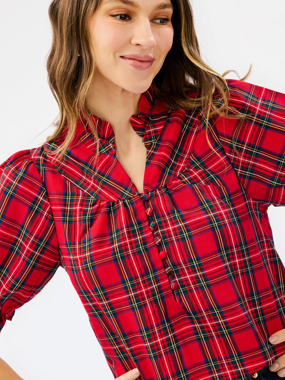 A woman wearing a red plaid button-up blouse with green and yellow intersecting lines, photographed against a plain light background.