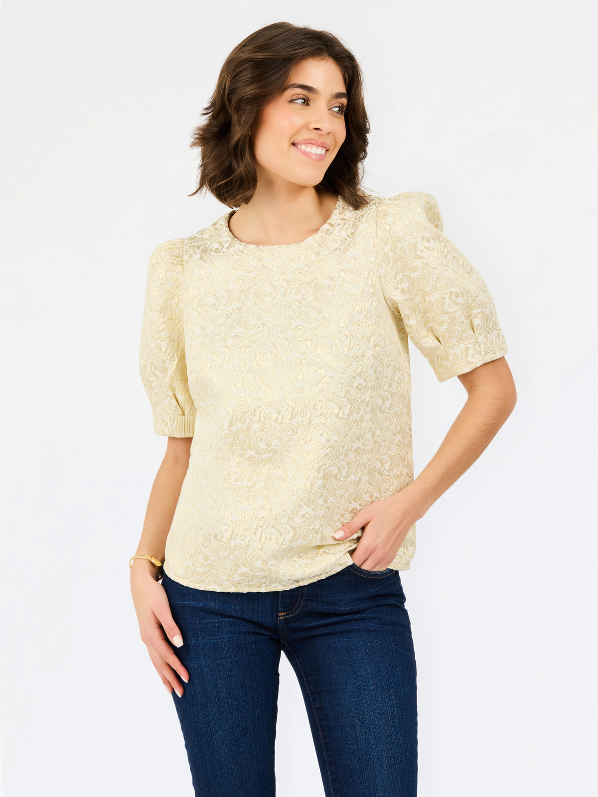 A woman wearing a pale yellow textured short-sleeve blouse with puff sleeves and dark blue jeans, standing against a plain white studio background.