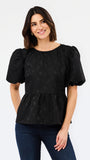 A woman modeling a black short-sleeve blouse with textured puff sleeves and a peplum waist, paired with dark blue jeans, against a plain white studio background.