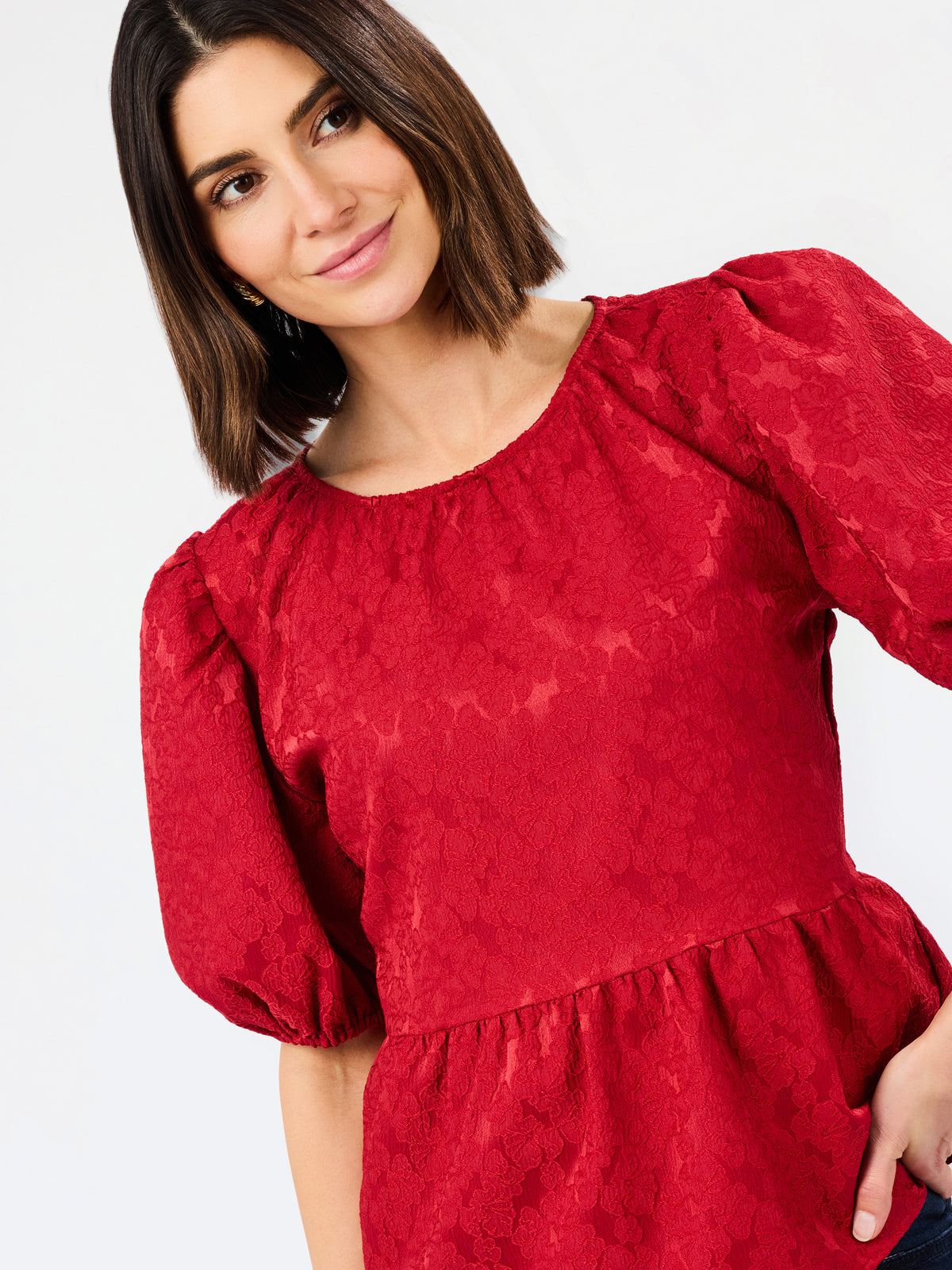 A woman wearing a red textured puff-sleeve top with a gathered waist, photographed against a plain light background.