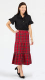 A woman modeling a black short-sleeve collared shirt and a red tiered plaid midi skirt with black heels, photographed against a light gray studio background.