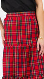 A close-up of a model wearing a red tiered plaid skirt with green, yellow, and white stripes, paired with a black top against a plain white background.