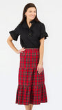 A woman modeling a black short-sleeve button-up shirt with ruffled sleeves and a high-waisted red and black plaid tiered midi skirt, set against a plain white studio background.