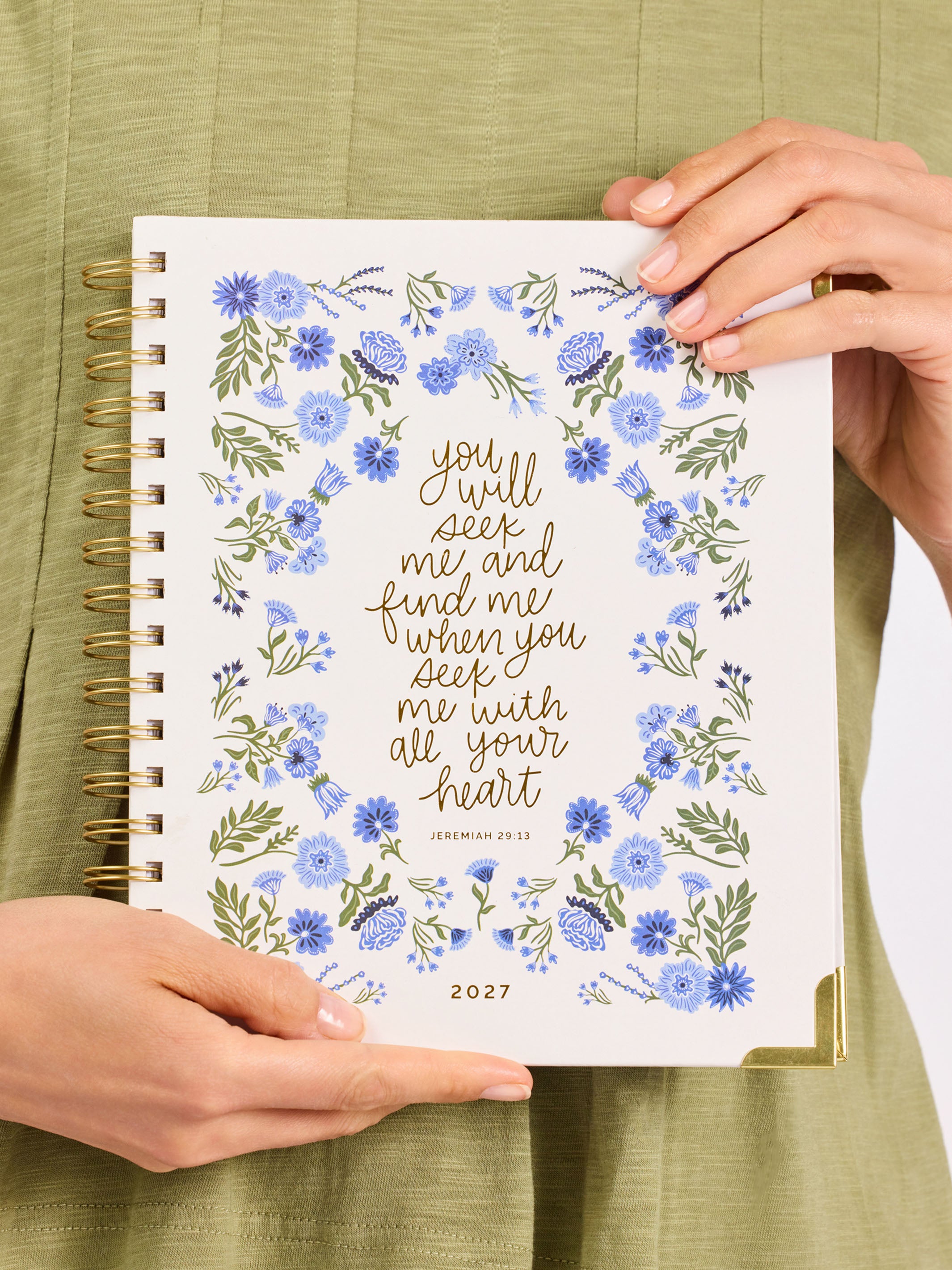 Person holding a 2027 planner with floral design and text on a green background