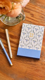 Notebook with floral design, pen, and flowers on a wooden surface