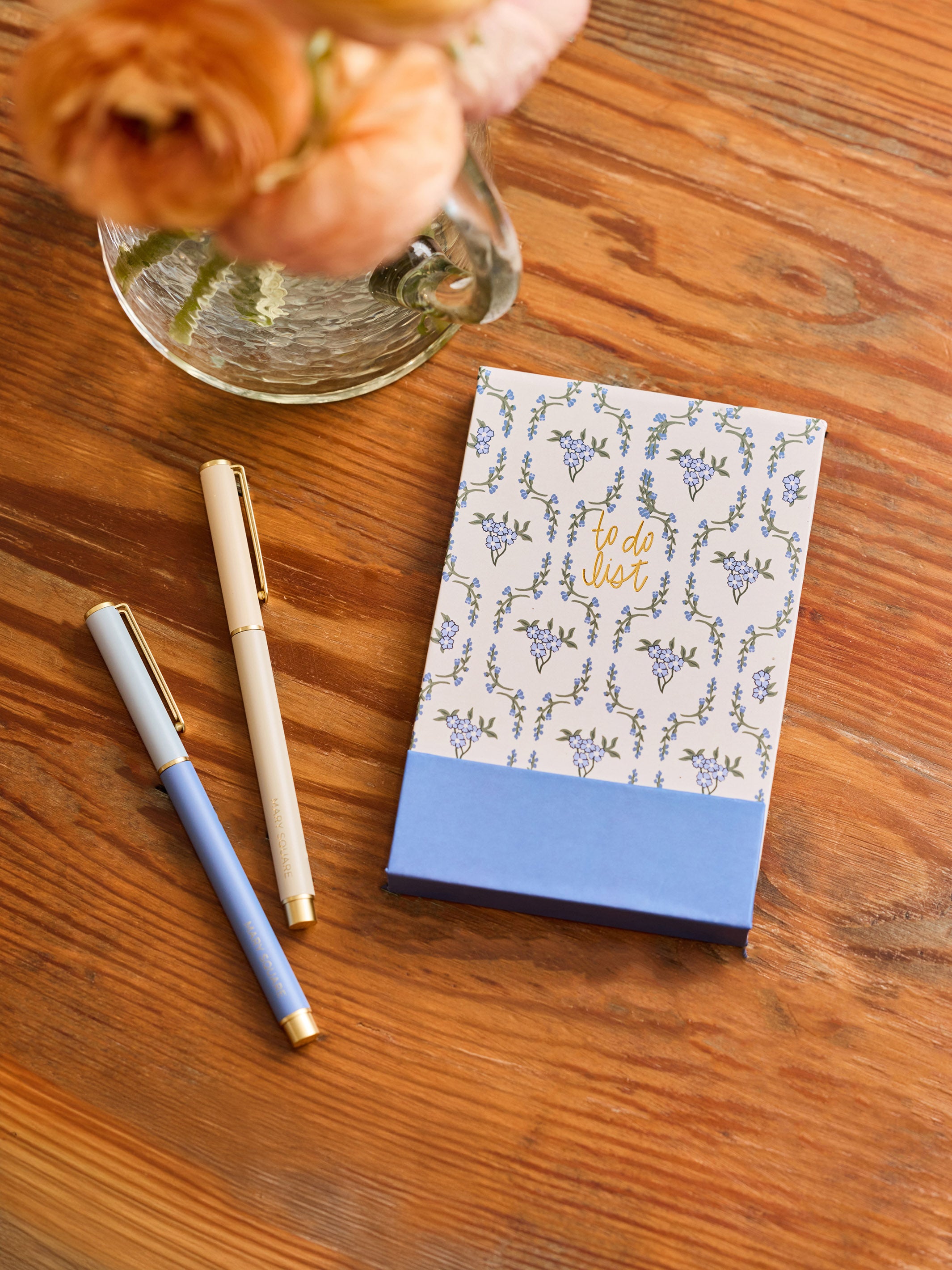 Notebook with floral design, pen, and flowers on a wooden surface