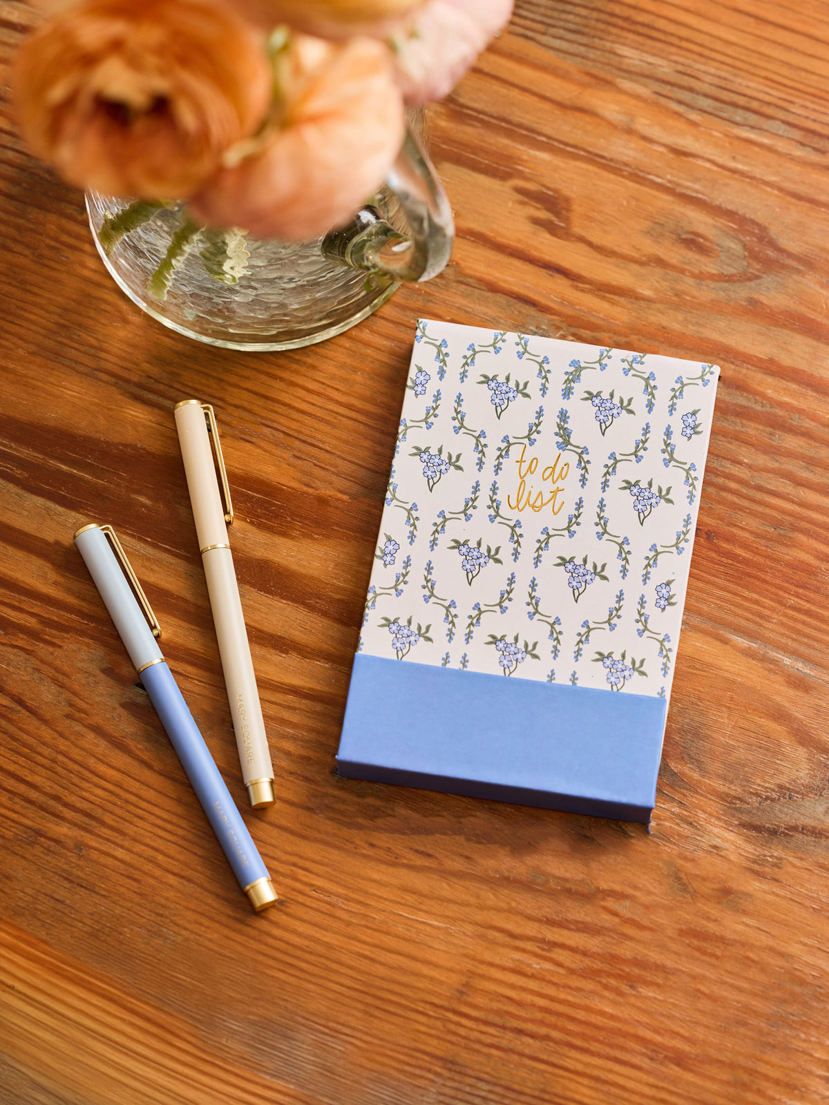 Notebook with floral design, pen, and flowers on a wooden surface
