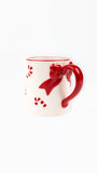 A white ceramic mug with a glossy red handle shaped like a bow, red rim, and red candy cane cutouts on the side, shown against a plain white background.