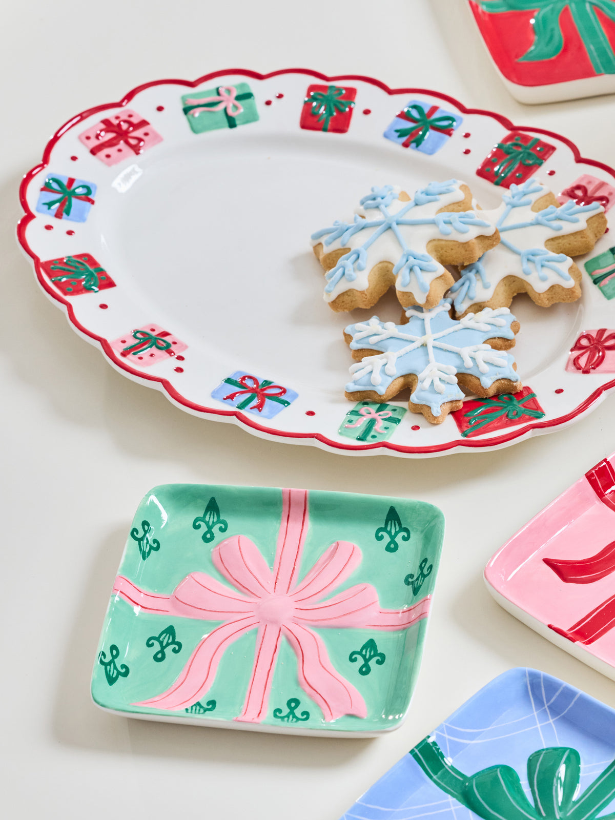 A set of ceramic holiday serving dishes with festive gift-wrap patterns, shown styled with snowflake-shaped cookies on a white background.