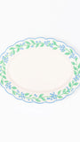 An oval ceramic serving platter with a scalloped rim, featuring a delicate border pattern of green leaves and small blue flowers on a white background.