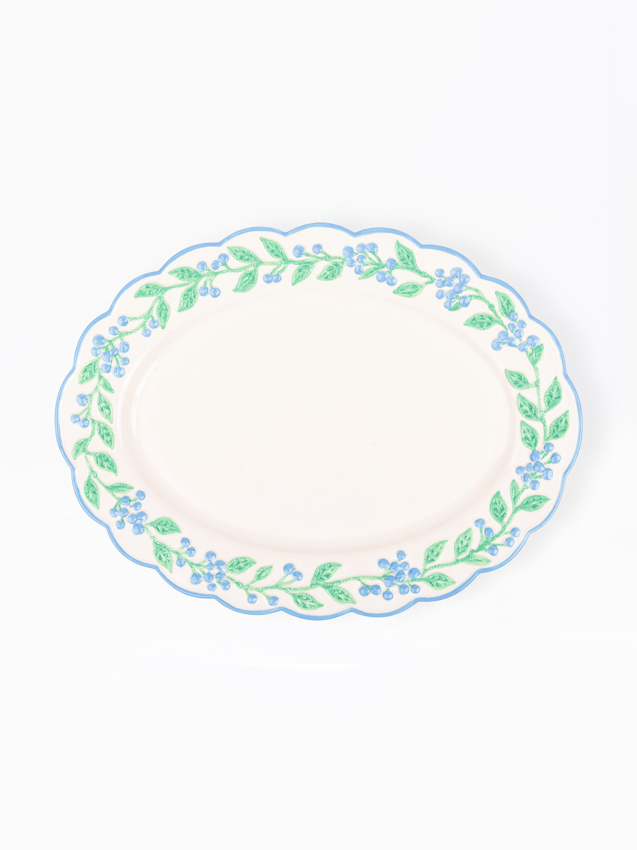 An oval ceramic serving platter with a scalloped rim, featuring a delicate border pattern of green leaves and small blue flowers on a white background.