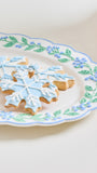 Snowflake-shaped sugar cookies decorated with light blue and white icing, served on a white ceramic plate with a blue and green floral border.