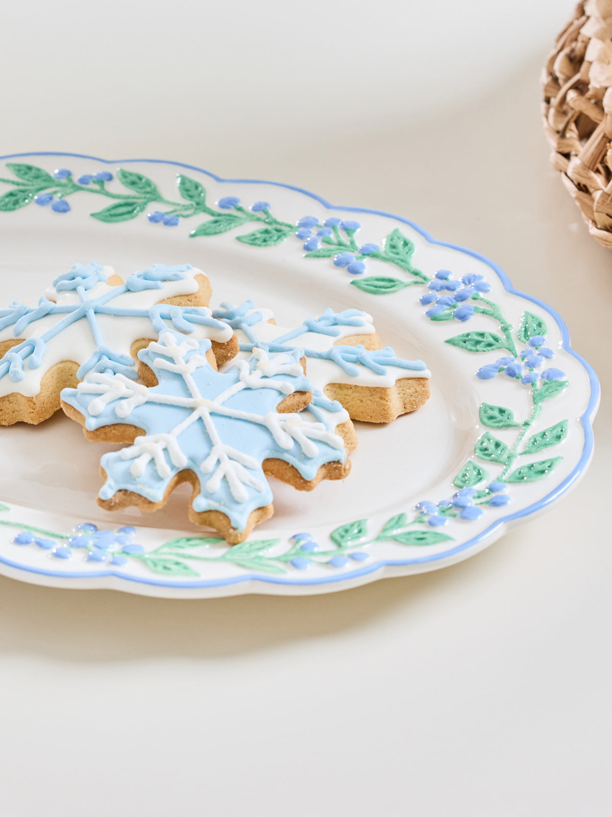 Snowflake-shaped sugar cookies decorated with light blue and white icing, served on a white ceramic plate with a blue and green floral border.