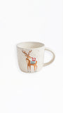 A cream-colored ceramic mug featuring a brown reindeer illustration wearing a red Santa hat and a green patterned scarf, set against a plain white background.