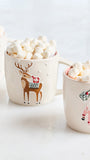 Three cream-colored ceramic mugs filled with marshmallows on a white surface. The center mug features a brown reindeer wearing a red and green sweater, and the right mug shows a pink Santa Claus.