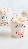 Three cream-colored ceramic mugs filled with marshmallows and hot chocolate, decorated with festive holiday illustrations including a Christmas tree, Santa Claus, and a reindeer.