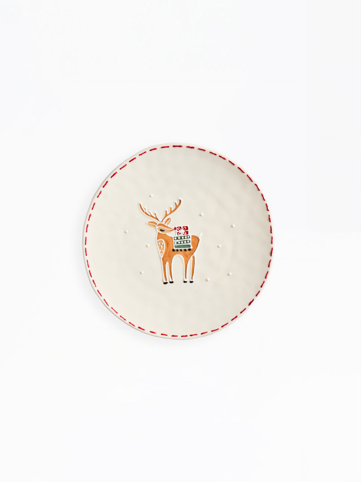 A round off-white ceramic plate featuring a central illustration of a brown reindeer with a colorful holiday sweater and the word 'MERRY'. The plate has a red dashed border and is photographed against a clean white background.