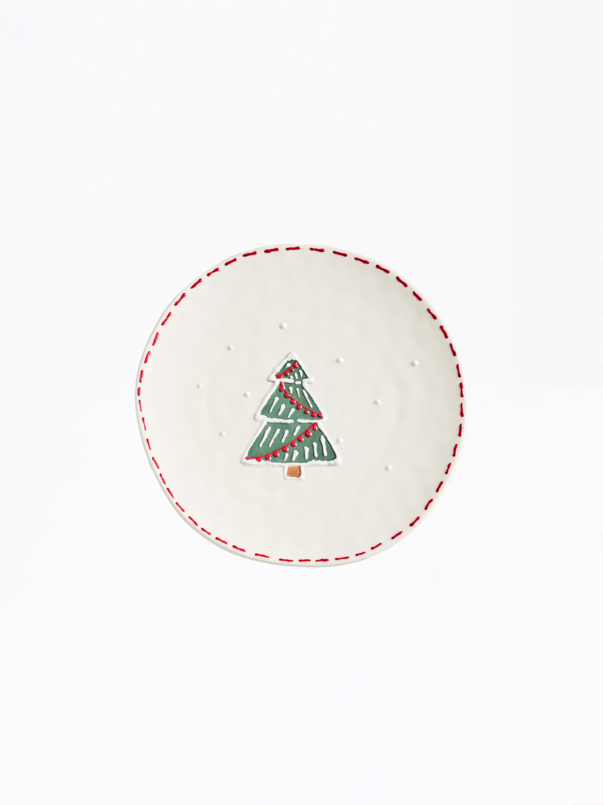 A round white ceramic plate featuring a hand-painted green Christmas tree with red stripes and a red dashed rim, shown against a plain white background.