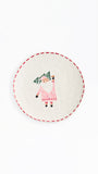 A round white ceramic plate featuring a hand-painted illustration of a Santa Claus figure holding a green Christmas tree, framed by a red dashed border on a white background.
