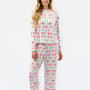 A woman modeling a matching two-piece pajama set with a long-sleeve top and wide-leg pants, featuring an all-over repeating bow pattern in red, green, and blue on a white background.