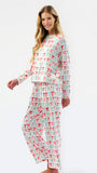 A woman modeling a matching long-sleeve pajama set with a white base and an allover print of small red and green bows, photographed against a plain white studio background.