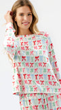 A woman modeling a matching long-sleeve top and pants pajama set with a colorful repeating bow pattern on a white background.