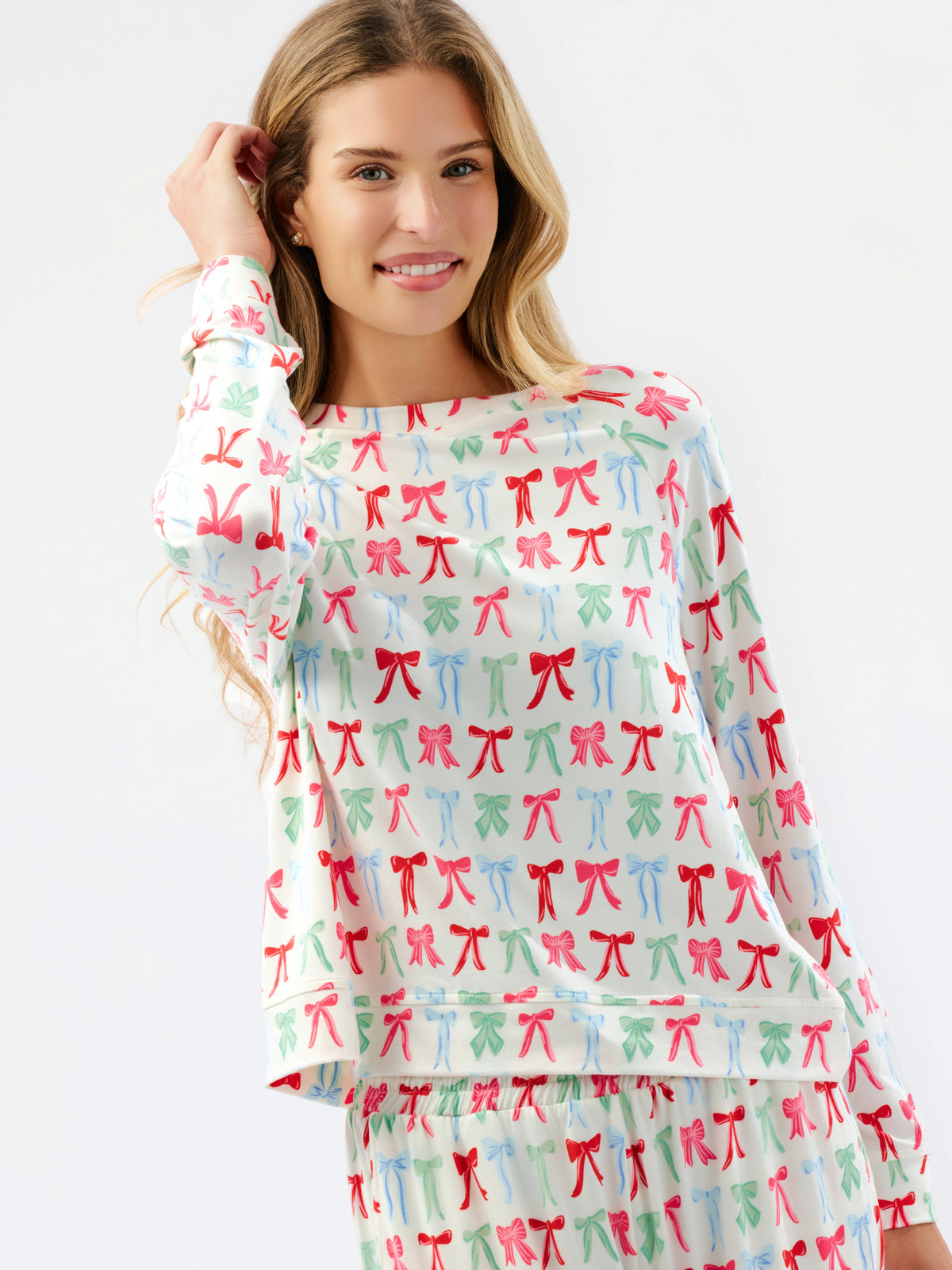 A woman modeling a matching long-sleeve top and pants pajama set with a colorful repeating bow pattern on a white background.