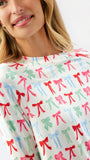 A close-up of a woman wearing a white long-sleeve top with an all-over repeating pattern of colorful bows in red, green, and light blue.