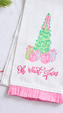 A white kitchen towel with a pink ruffled hem, featuring a colorful embroidered Christmas tree, presents, and the phrase 'Oh what fun' in pink script.