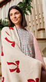 A woman wrapped in a cream knit blanket with red bow patterns, standing on a decorated indoor staircase.