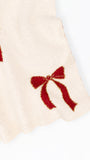 Close-up of a cream-colored knit fabric with red glittery bow patterns, shown against a plain white background.